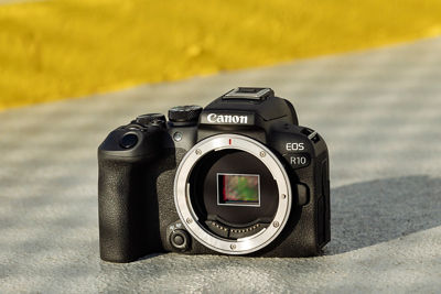A Canon EOS R10 sitting on a grey surface with a faint checked pattern, with no lens fitted so that the camera's sensor is showing.